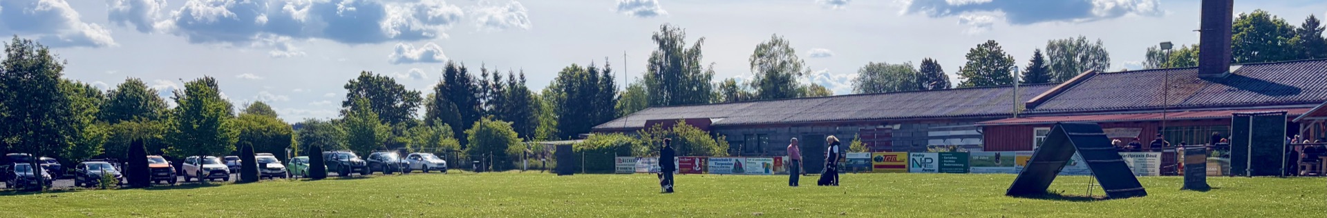 Panoramablick auf das Trainingsgelände des HSV Reichenbach mit Vereinsheim, Hindernis und Mitgliedern beim Training